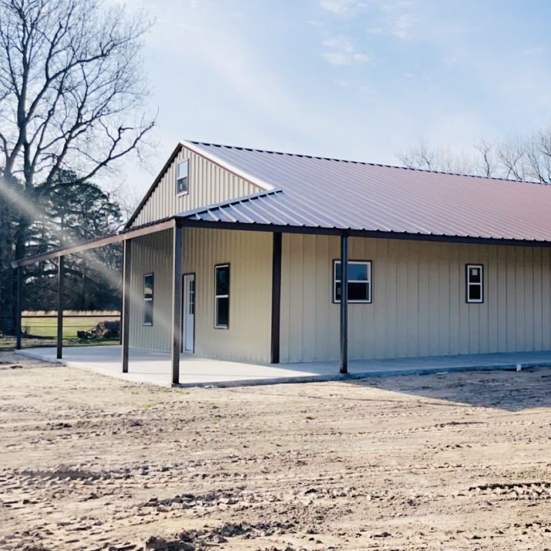 A small building with a metal roof and a red roof, standing alone in a serene setting.